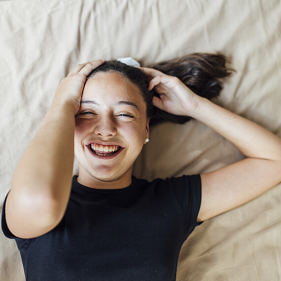 Pre-adolescent girl hands in hair lying on bed at home